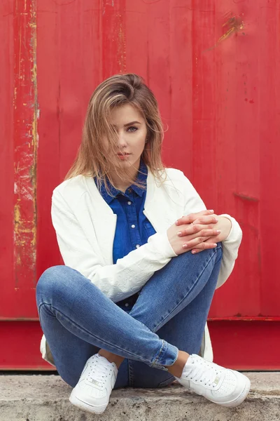 Красивая девушка сидит на земле возле стены в джинсы и белая блузка, ее волосы развивается Ветер — стоковое фото