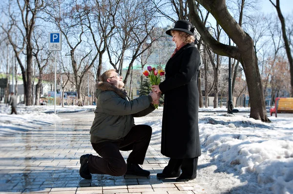 Старый летний мужчина дарит цветы его женщине, Приседания на одной ноге — стоковое фото