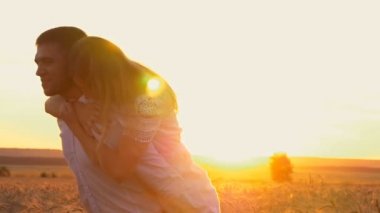 Молодая красивая пара девочка и мальчик, играя и флирт в пшеничном поле на закате. Парень держит девушка на спине — стоковое видео