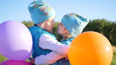Две сестры-близнецы обниматься и целоваться. Дети держать шары — стоковое видео