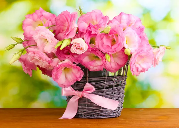 Букет из эустомы цветов в плетеной вазе, на деревянном столе, на зеленом фоне — стоковое фото